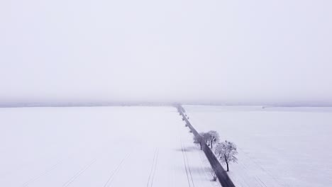 Flying-along-a-straight-road-cutting-through-snow-covered-farmland