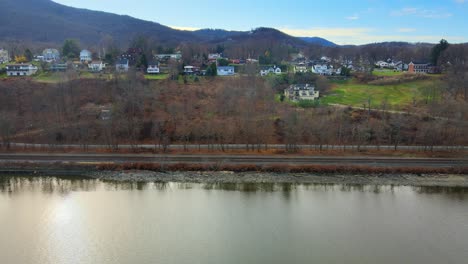 Drone-flying-sideways-past-a-small,-picturesque-village-in-New-York-on-the-banks-of-a-river-with-a-mountain-backdrop