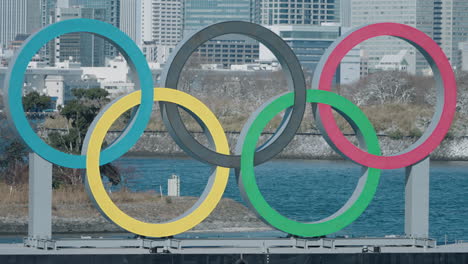 Olympic-Rings-Monument-Reinstalled-At-Odaiba-Marine-Park-With-Cityscape-In-Background-In-Minato,-Tokyo,-Japan