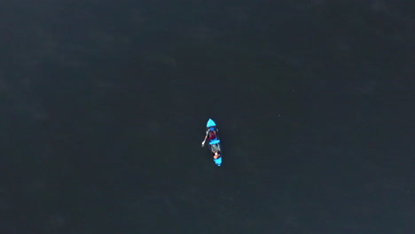 Drone-aerial-footage-of-topdown-kayak-with-people-slowly-paddling-on-a-calm,-relaxing-lake