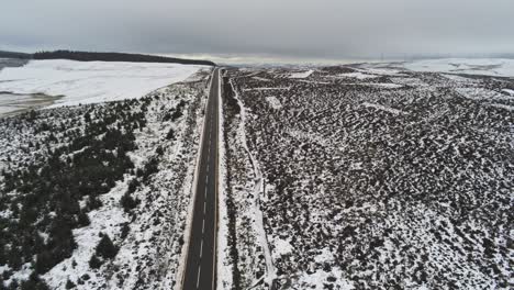 Long-road-aerial-into-distance-across-highland-snowy-countryside-moors-high-to-low