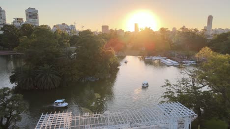 Aerial-dolly-out-of-Rosedal-gardens-pond-with-white-bridge-and-Palermo-Woods-pedestrian-street-at-sunset,-Buenos-Aires