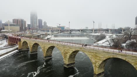 People-Walking-on-Stone-Arch-Bridge-in-Minneapolis,-Minnesota-on-Foggy-Winter-Morning
