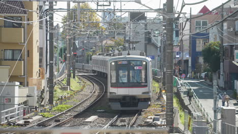 Jr-Zug-Nähert-Sich-Dem-Bahnhof-Mit-Einheimischen,-Die-An-Einem-Sonnigen-Tag-In-Japan-In-Der-Straße-Von-Tokio-Spazieren-Gehen