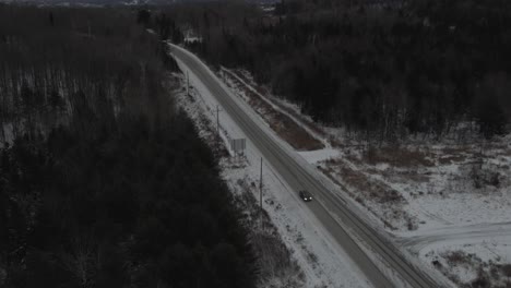 Car-Driving-On-Snowy-Highway-With-Bare-Trees-On-A-Winter-Sunrise---aerial-drone,-tilt-down