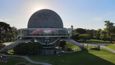 Aerial-dolly-in-of-Galileo-Galilei-Planetarium-and-people-resting-in-Palermo-Woods-at-daytime,-Buenos-Aires