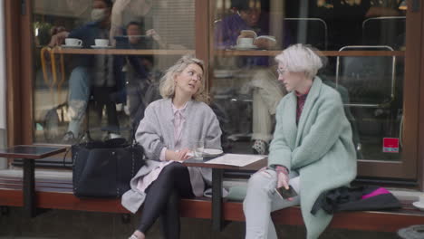 Dos-Mujeres-Caucásicas-Hablando-Mientras-Están-Sentadas-Afuera-De-Una-Cafetería-En-Tokio,-Japón,-Cuando-Hace-Buen-Tiempo