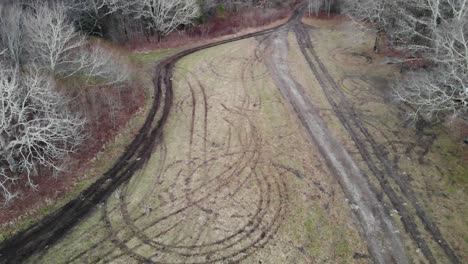 tire-tracks-in-grass-field-in-forest-aerial-drone-tilt-descending