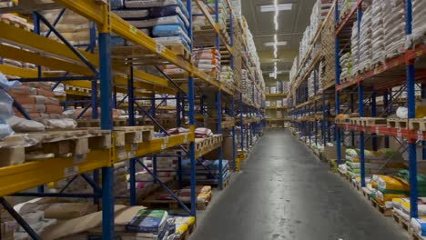 Panning-shot-of-long-indoor-warehouse-depot-with-lights-and-storage-racks-full-of-products