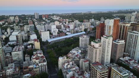 Dolly-in-flying-over-Barrancas-de-Belgrano-park-and-train-station-surrounded-by-buildings-at-sunset,-Buenos-Aires,-Argentina