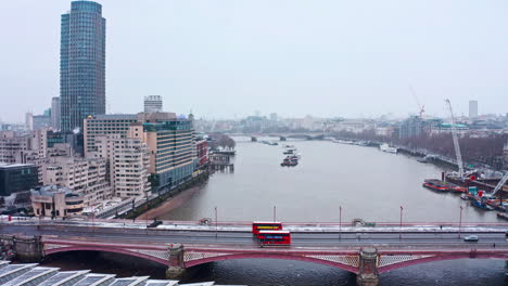 Dolly-forward-aerial-drone-shot-of-red-London-buses-on-Blackfriars-bridge-in-the-snow