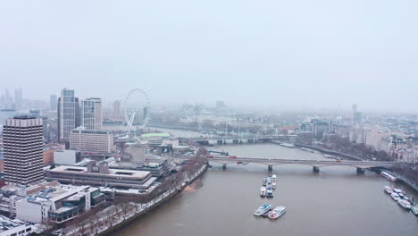 Cinematic-rotating-aerial-shot-of-snow-falling-London-waterloo-bridge-south-bank-London-eye