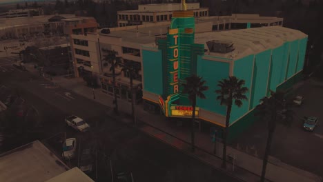Filmische-Top-City-Luftaufnahme-Der-Innenstadt-Von-Roseville,-Kalifornien,-Mit-Industriegebäuden,-Geschäften-Und-Tower-Theatre-Neben-Einer-Mehrstöckigen-Parkplatzstruktur-Während-Des-Sonnenuntergangs-Und-Vorbeifahrender-Autos
