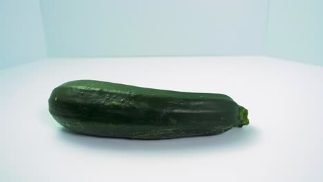 Grüner-Frischer-Zucchini-Kürbis-Dreht-Sich-Auf-Hellblauem-Hintergrund,-Gesundes-Essen,-Konzept,-Mittlere-Nahaufnahme-Der-Kamera-Dreht-Sich-Nach-Rechts