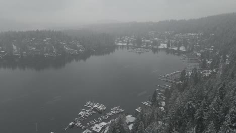 White-Snow-falling-down-over-green-pine-trees-and-marina-with-small-boats-docked-in-Deep-Cove-Bay-in-British-Colombia-on-a-cold-cloudy-winter-day