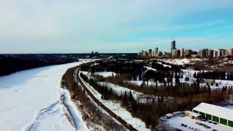 aerial-winter-flyover-the-Royal-Glenora-Club-next-to-Victoria-Park-Ice-Skating-track-rink-by-the-forest-next-to-snow-covered-North-Saskatchewan-River-with-the-Pearl-condominium-skylline-horizon-1-2