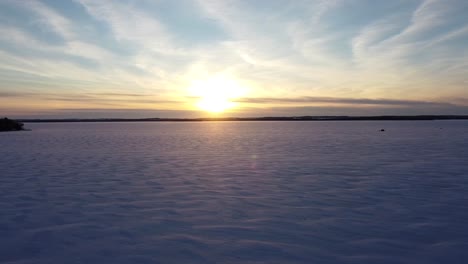 Sunset-over-vast-snow-covered-frozen-lake-with-ice-fishing-huts-during-winter