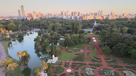 Aerial-dolly-out-of-people-walking-in-Palermo-Woods-street,-Rosedal-gardens-and-pond-at-sunset,-Buenos-Aires