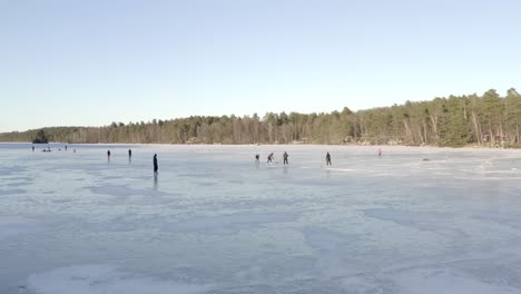 Eine-Gruppe-Von-Menschen,-Die-Auf-Einem-Großen-Zugefrorenen-See,-Umgeben-Von-Hohen-Grünen-Bäumen,-Eishockey-Spielen