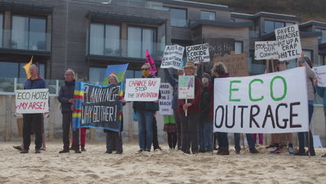 Protesters-stand-together-on-the-beach-in-front-of-the-Carbis-Bay-Hotel-in-St-Ives,-Cornwall-holding-signs-and-placards-in-demonstration