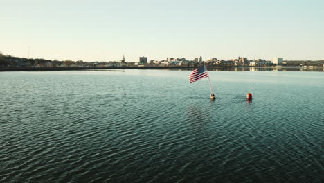 Aerial-of-a-Flag-flying-in-the-wind-attached-to-a-buoy-with-Portland-Maine-skyline-visible-in-the-background