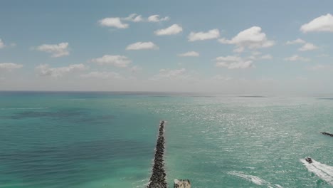 Aerial-view-of-the-ocean-in-Miami-Beach,-a-boat-sails-towards-the-ocean-between-breakwaters,-near-South-Pointe-Beach,-slow-motion