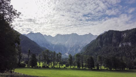 Kamnik-Savinja-Alps-from-Jezersko,-Slovenia,-Timelapse-of-clouds-above-mountains-and-meadows-with-trees-in-front