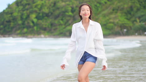 Schöne-Asiatische-Frau,-Die-Am-Strand-Der-Insel-In-Der-Nähe-Des-Meeres-Spazieren-Geht-Und-Bluse-Und-Jeansshorts-Trägt