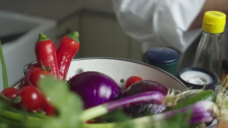 Chef-hand-picks-up-cucumber-from-bowl-with-vegetables-on-a-kitchen-table