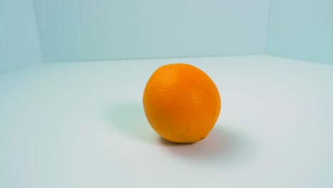 Frische-Große-Saftige-Orange-Dreht-Sich-Langsam-Auf-Hellblauem-Hintergrund,-Gesundes-Lebensmittelkonzept,-Nahaufnahme,-Kamera-Dreht-Sich-Nach-Links