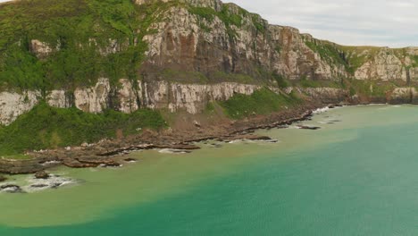 Zooming-out-orbiting-shot-of-a-cliff-along-the-coast-in-New-Zealand-during-the-day