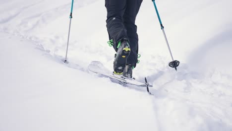 Close-up-view-of-skier-walking-uphill-with-poles-in-a-snow-landscape