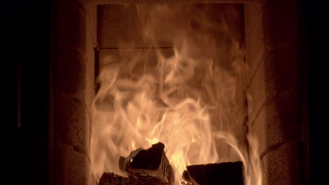 Dolly-shot-across-the-inside-of-a-log-burning-fireplace-with-high-flames,-bright-golden-orange-flames