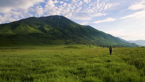Single-person-hiking-in-lush-green-mountainous-meadow-on-a-beautiful-summers-day,-static-shot