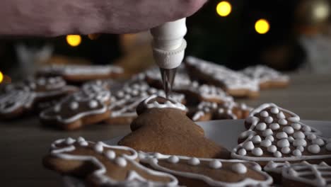 Male-chef-decorating-gingerbread-tree-with-white-sugar-icing-with-Christmas-tree-in-the-background