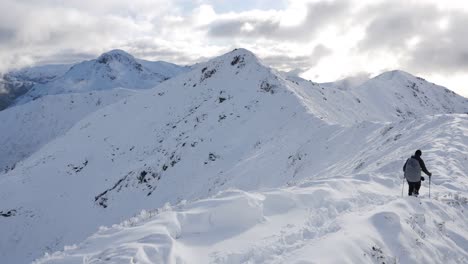 Woman-hiker-on-a-breathtaking-landscape-crossing-a-snowy-ridge-in-the-Fiodrland,-New-Zealand