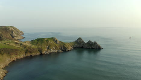 Beautiful-drone-footage-of-three-cliffs-bay-with-calm-sea-at-sunset-in-Gower-peninsula,-South-Wales