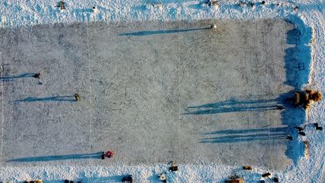 Winterluftvogelblick-Halten-über-Künstlicher-Mehrzweck-Eisbahn-Bei-Schneebedecktem-Park-Sonnenuntergang,-Während-Eltern-Dem-Kind-Beibringen,-Mit-Dreiecksunterstützung-Schlittschuh-Zu-Laufen,-Andere-üben-Hockey,-Ein-Anderer-Versucht-Eiskunstlauf-2-3