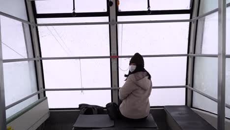 Girl-inside-snowy-cable-car-skiing-while-wearing-facemask