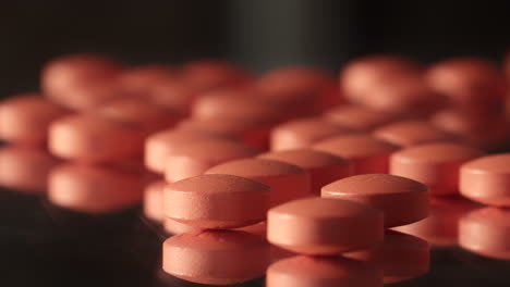 Many-small-pink-red-prescription-drug-pills-tablets-spilled-across-dark-mirrored-surface-close-up