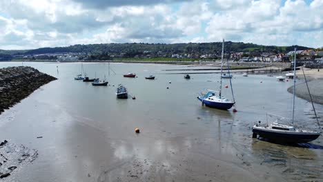 Aerial-view-moored-boats-on-Welsh-low-tide-seaside-breakwater-harbour-coastline-slow-fly-over