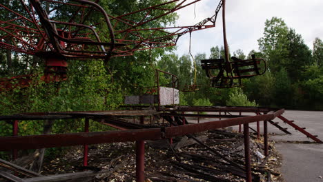 Broken-swing-ride-spinning-on-windy-day-in-Pripyat-amusement-park,-zoom-in