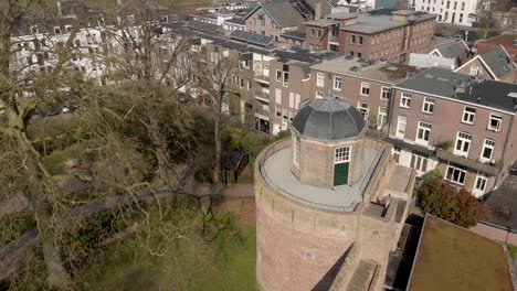 Slow-sideways-descend-showing-top-of-historic-Bourgonje-stronghold-tower-and-city-wall-with-park-landscape-in-Zutphen,-The-Netherlands