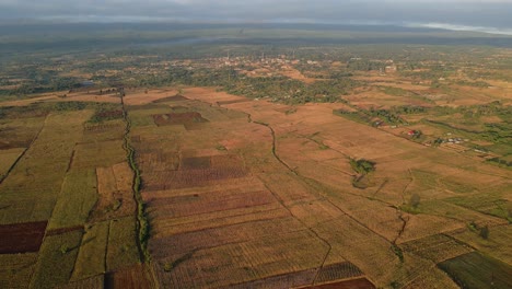 Vista-Aérea-De-Tierras-De-Cultivo-Iluminadas-Por-El-Sol,-Tarde-En-África-Rural---Reversa,-Disparo-De-Drones