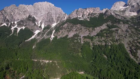 Epic-mountain-ridge,-glacier-white-snow-on-slopes-of-rocky-alps-and-green-wild-forests-in-Albania