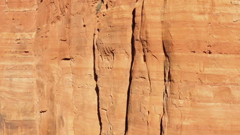Sandstone-formation-rock-mountain-wall-in-sunlight-at-Sedona,-Arizona---tilt-up-shot-drone-shot