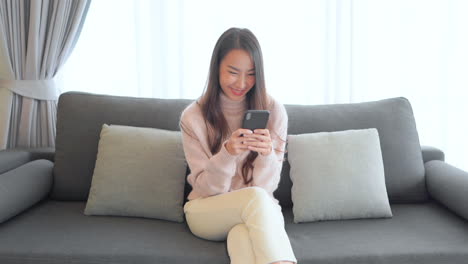 Happy-Woman-typing-on-a-smartphone-with-two-hands-Asian-adult-in-casual-clothes-sitting-on-the-sofa-and-typing-with-both-hands-message-in-mobile-phone