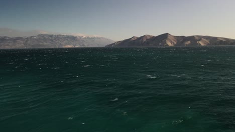 Aerial-plane-with-dolly-out-at-low-altitude-over-the-Adriatic-Sea-and-on-the-horizon-large-Croatian-mountains-in-the-center-of-the-plane-divide-majestically-4k