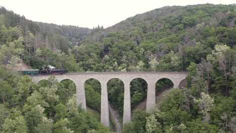 Steam-train-passing-over-a-stone-viaduct-in-a-mountain-valley,zooming