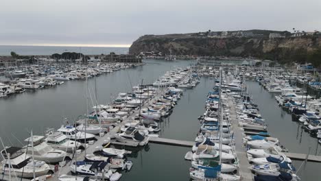 Aerial-drone-view-over-yachts,-at-the-Dana-Point-Marina,-in-dark,-cloudy-California,-USA